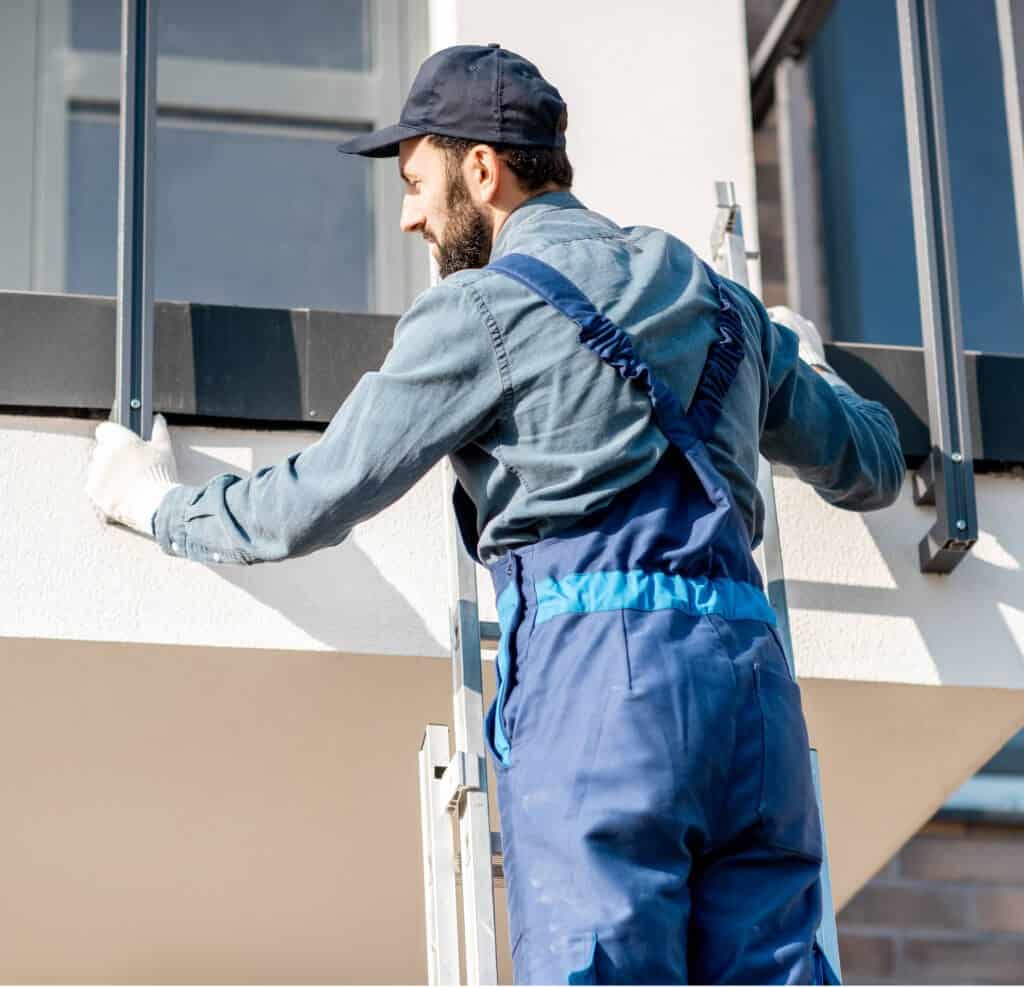 Construction worker on ladder installing balcony fence. Home improvement and building concept.